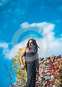 Stylish handsome macho man standing against sky and colorful ivy leaves. Man lifestyle. Man fashion and wellness concept