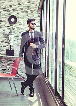 Stylish handsome man wearing fancy clothes sunglasses. indoor fashion portrait. clothing red chair. Buddha in background