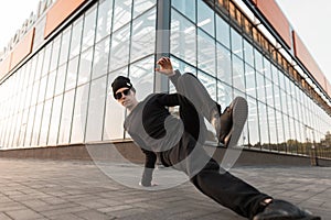 Stylish handsome young hipster man in fashionable dark sunglasses in trendy black clothes dancing break dance