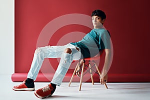 Stylish handsome young man relax and posing on studio sitting on a chair looking to camera.
