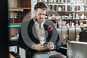 Stylish handsome young man using smartphone while sitting