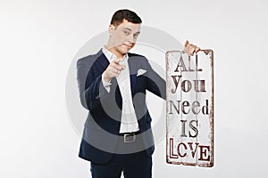 Stylish and handsome young man a in a white shirt and dark blue suit holds a big sign in his hand and posing at white