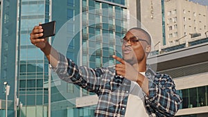 Stylish happy african man in trendy sunglasses speaks webcam mobile phone in city. Afro american male blogger vlogger