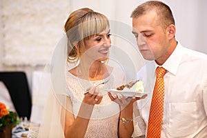 stylish happy bride and groom cutting and tasting fabulous wedding cake in a restaurant