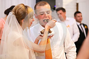 stylish happy bride and groom cutting and tasting fabulous wedding cake in a restaurant