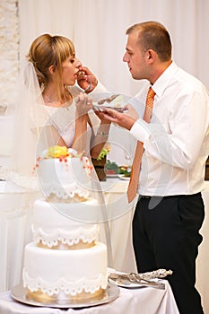 stylish happy bride and groom cutting and tasting fabulous wedding cake in a restaurant