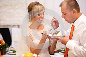 stylish happy bride and groom cutting and tasting fabulous wedding cake in a restaurant