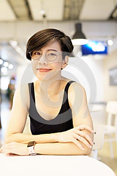 Stylish, happy and confident short hairstyle Asian woman wear eyeglasses, smiling, sitting, looking at camera in modern cafe