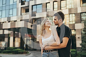 Stylish happy couple hugging on urban background, looking at each other and smiling. Street portrait of a loving couple on a walk