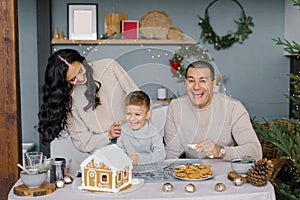 A stylish happy family decorates a gingerbread house