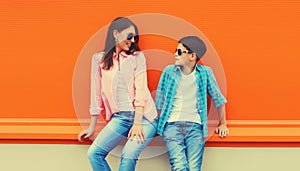 Stylish happy smiling mother with son teenager look at each other posing together in sunglasses, checkered shirts, jeans in the
