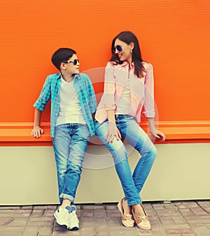 Stylish happy smiling mother with son teenager look at each other posing together in sunglasses, checkered shirts, jeans in the