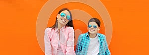 Stylish happy smiling mother with son teenager posing together in sunglasses, checkered shirts, jeans in the city on orange