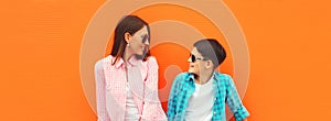 Stylish happy smiling mother with son teenager posing together in sunglasses, checkered shirts, jeans in the city on orange