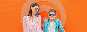 Stylish happy smiling mother with son teenager posing together in sunglasses, checkered shirts, jeans in the city on orange