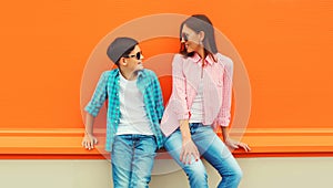 Stylish happy smiling mother with son teenager posing together in sunglasses, checkered shirts, jeans in the city on vivid orange