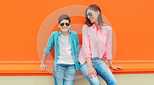 Stylish happy smiling mother with son teenager posing together in sunglasses, checkered shirts, jeans in the city on vivid orange