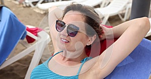 Stylish happy young woman in swimsuit and sunglasses enjoying life reboot on beach lounger by pool during summer