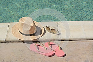 Stylish hat, flip flops and sunglasses near outdoor swimming pool on sunny day. Beach accessories