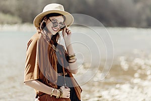 stylish hipster boho woman smiling in sunglasses with hat, leather bag, fringe poncho and accessory. happy traveler girl look, ne