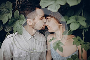 Stylish hipster bride and groom kissing in green leaves, holding