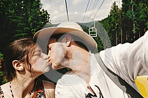 Stylish hipster couple kissing on chairlift in summer mountains