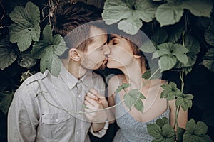 Stylish hipster couple kissing in green leaves, holding hands. m