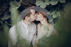 Stylish hipster couple kissing in green leaves, holding hands. m