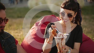 Stylish hipster couple sitting eating ice cream and waffles laughing in city park. Romantic young man and woman having