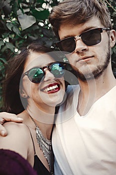 Stylish hipster couple in sunglasses smiling and making cool selfie. Happy family couple in love making self portrait and laughing