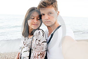 Stylish hipster couple taking selfie on beach at evening sea. Summer vacation. Portrait of happy young family on honeymoon on