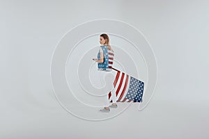 Stylish hipster girl in american patriotic outfit holding big us flag isolated on grey