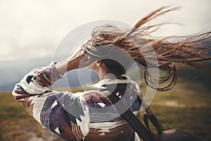 Stylish hipster girl with backpack and windy hair on top of mountains. Portrait of happy young woman relaxing. Carefree mood.