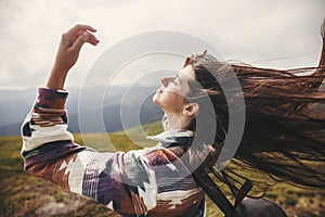 Stylish hipster girl with backpack and windy hair on top of mountains. Portrait of happy young woman relaxing. Carefree mood.