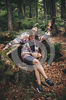 Stylish hipster girl having fun and relaxing in forest in mountains. Young woman traveler exploring woods. Eco holiday. Travel and