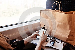 stylish hipster girl holding phone with headphones at window light in train. travelling by train concept. beautiful young woman l