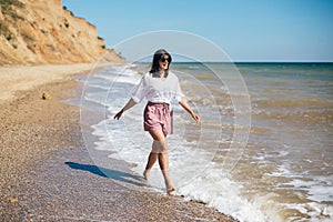 Stylish hipster girl relaxing on beach and having fun.  Happy young boho woman walking and smiling in sea waves in sunny warm day