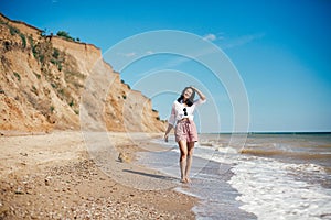 Stylish hipster girl relaxing on beach and having fun.  Happy young boho woman walking and smiling in sea waves in sunny warm day