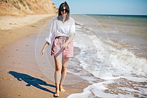 Stylish hipster girl  walking on beach and smiling. Summer vacation. Happy young boho woman relaxing and enjoying sunny warm day