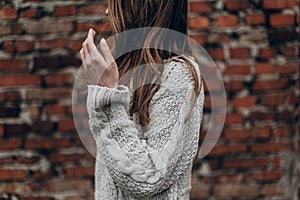 stylish hipster gypsy woman posing in knitted sweater on background of brick wall, holding hair. atmospheric sensual moment.