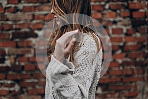 stylish hipster gypsy woman posing in knitted sweater on background of brick wall, holding hair. atmospheric sensual moment.