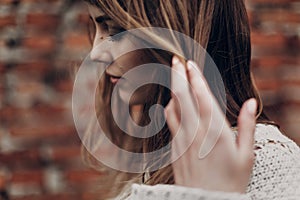 stylish hipster gypsy woman posing in knitted sweater on background of brick wall, holding hair. atmospheric sensual moment.