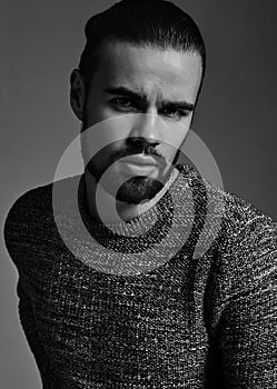 Stylish hipster lumbersexual model dressed in warm sweater posing in studio