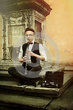 Stylish hipster man playing clarinet on background of old city s