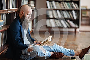Stylish hipster man reading book sitting on floor in library