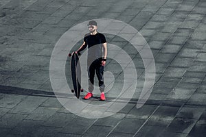 Stylish hipster man standing with a longboard on concrete tiles