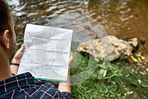 Stylish hipster traveler exploring map at forest and lake in the mountains