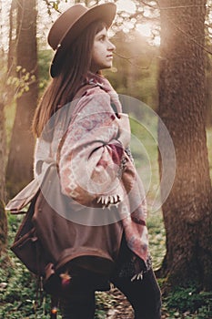 stylish hipster traveler girl in hat with backpack walking in woods in evening sunshine. bohemian fashionable woman exploring in