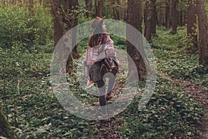 stylish hipster traveler girl in hat with backpack walking in woods in evening sunshine. bohemian fashionable woman exploring in