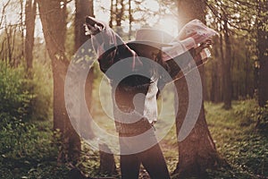 stylish hipster traveler girl in hat exploring in woods in amazing evening sunshine light. woman having fun and jumping in